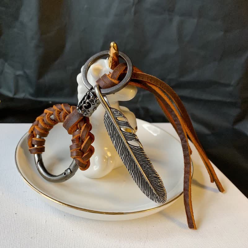 Portachiavi in ​​pelle intrecciata con piuma in metallo vintage e nappa